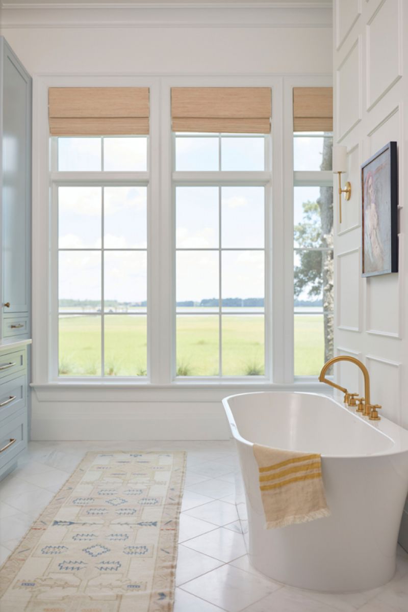 Viewfinder: Situated on the ground floor, the primary suite captures views of the marsh and the Ashley River beyond. A freestanding tub accented by a brass California Faucets fixture offers a sublime spot to soak up the scenery. Cabinets painted in Farrow and Ball “Parma Gray” are complemented by walls hand-painted by local artist Marian Pouch.