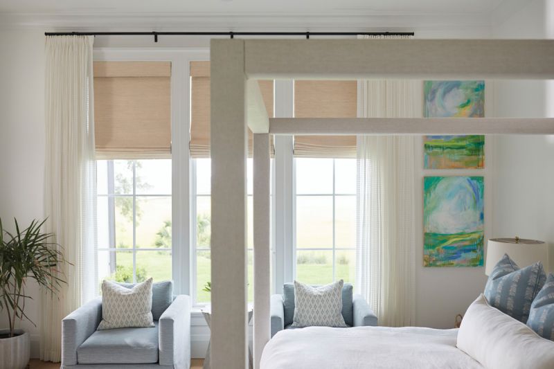 Serene Dream: The light-filled primary bedroom features an upholstered four-poster bed and Thibaut Design chairs. Artwork by Holland Sharon adds a pop of color to the peaceful space.