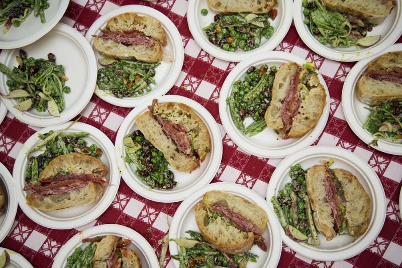 Sandwiches piled with salami cotta from Keegan-Filion, provolone, lettuce, tomato, AMS sauce, and focaccia are paired with an English pea salad featuring peanuts, green garlic, buttermilk dressing, peas from Rosebank Farms, and radishes from Rebellion Farms.