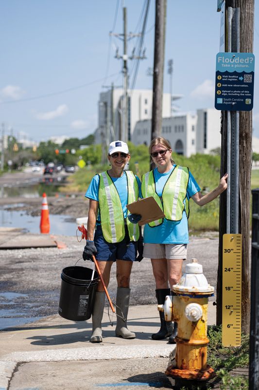 Sara McDonald and Kelly Thorvalson of the SC Aquarium near one of 11 downtown signs encouraging passersby to report flooding through the Sea Rise portal.