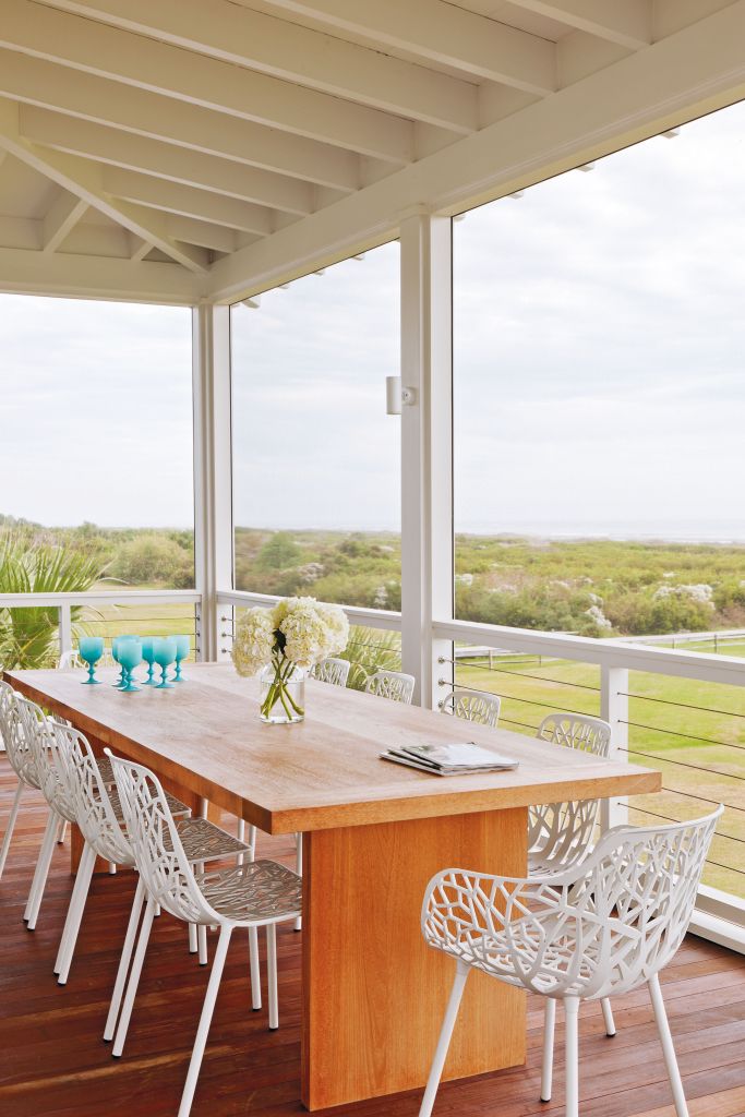 <strong>Dinner with a View</strong> - Designer Jenny Keenan enlisted Brian Hall of Kistler Design Co. to craft this custom teak table with an organic look that perfectly suits this sleek deck and provides a clean backdrop for branch-patterned chairs. Trading wire for more commonly used wood or metal railings gives a nearly uninterrupted view of the surrounding maritime scrub and ocean in the distance. <strong>Location:</strong> Sullivan’s Island <strong>Issue:</strong> July 2014, “The Art of Summer” <strong>Photographer:</strong> Julia Lynne  <a href="https://charlestonmag.com/features/the_art_of_summer"><strong>&gt;&gt;CLICK HERE TO READ THE ARTICLE</strong></a>