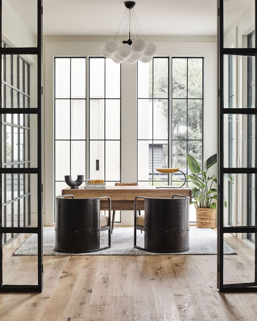 <strong>Curve Appeal </strong>- Iron barrel-back chairs and a bulbous chandelier provide balance in this rectilinear iron and glass office. The washed walnut desk from Noir adds warmth. <strong>Location:</strong> Mount Pleasant <strong>Issue:</strong> November 2020, “Ship of Dreams” <strong>Photographer:</strong> Joseph Bradshaw  <a href="https://charlestonmag.com/features/tour_a_modern_industrial_home_located_on_the_site_of_a_historic_mount_pleasant_shipyard"><strong>&gt;&gt;CLICK HERE TO READ THE ARTICLE</strong></a>
