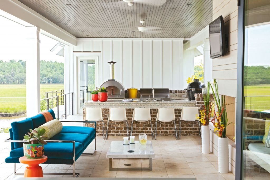 <strong>Under Cover</strong> - For this outdoor kitchen and living room, interior designer Deidre Alexander selected plastic Ikea chairs to line the brick bar (topped with Vetrostone), covered the low-slung sofa in a sturdy Silver State outdoor velvet, and tiled the floor in travertine. The result? The retreat looks great, rain or shine. <strong>Location:</strong> Daniel Island <strong>Issue:</strong> October 2013, “Wide Open Spaces” <strong>Photographer:</strong> Julia Lynn  <a href="https://charlestonmag.com/features/wide_open_spaces"><strong>&gt;&gt;CLICK HERE TO READ THE ARTICLE</strong></a>