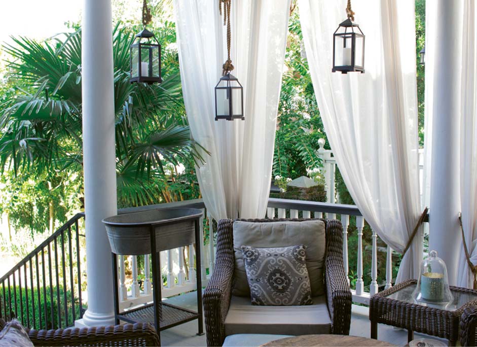 Scenic Overlook: Shaded by palm trees and sheer white curtains, the back porch is outfitted for year-round living with a whirring ceiling fan, a quartet of comfy wicker chairs, and a galvanized tub for icing drinks. “We’re out here constantly,” says Susan.